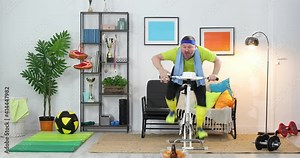 Young man on a stationary bike is exercising at home. Crazy cyclist rides for snack and beer. Unsporting guy training his bike at home. Funny sport Fitness parody. Humor. Sports comedy