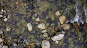 Top view of a waterbed full of rocks in different shapes and colors with a fast current in the water visible due to the white foam