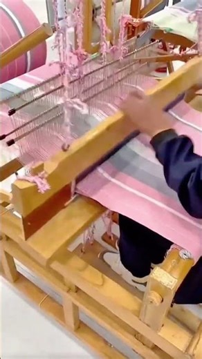 weaving pink and grey fabric using a traditional wooden loom and pulling shuttle to create textiles
