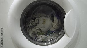 White washing machine washes dirty colorful clothes. Washing clothing in domestic washing machine. Close up video of spinning drum washing machine.