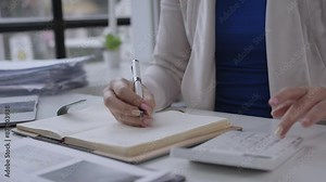 Professional businessperson working in an organized office environment, writing notes and using a calculator at a tidy desk. Focus on productivity and efficiency in a detailed oriented workspace