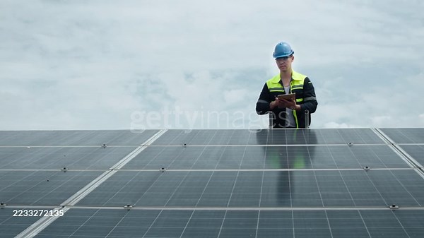 An engineer standing on a solar panel field using a digital tablet to...