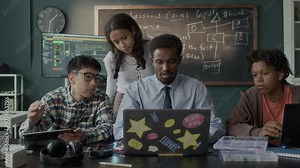 Medium shot of African American male teacher sitting in front of laptop and explaining software engineering topic to multiethnic group of students in class Stock Video