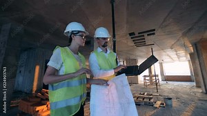 Building in construction with a female and a male builders, constructors, engineers walking along it
