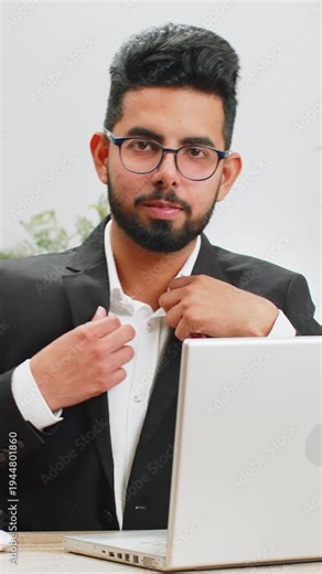 Portrait of happy smiling bearded Indian businessman at modern home office workplace desk look away turn head at camera. Male Hindu in formal suit. Handsome man remote distant online working on laptop