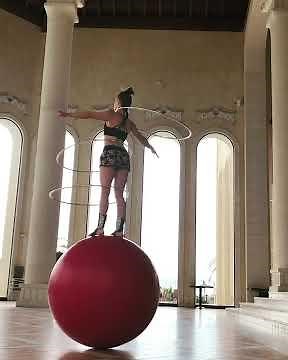 Woman Balances On Giant Yoga Ball And Performs With Multiple Hula Hoops -