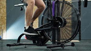 Legs of man pedal on spinning bike. Fit man training in modern gym using stationary bicycle. Sportsman spinning on cardio machine. Gym bike. Functional cardio training. 4K, UHD