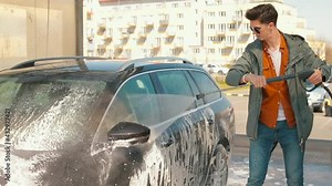 A man washes foam off a car using a high pressure spray bottle. It evenly waters the car module for cleaning. Preparing the vehicle for the trip.