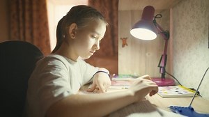 Education concept. Cute smart school child girl writing doing homework sit at home table. Teen girl doing school assignment. Happy child studying at home in the evening.