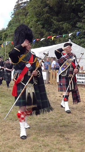 Drum Major Walter Davidson leads the salute to the Chieftains, as the combined pipe bands march past playing "Scotland the Brave" and then "Rowan Tree" during the 2024 Drumtochty Highland Games on Saturday 22nd June 2024. The Chieftains were Captain and Mrs Sheena MacBride and the bands were marching off after the official opening of the Games, held in the grounds of Drumtochty Castle at Auchenblae in Aberdeenshire, Scotland. Leading Drum Major Walter Davidson is followed by Drum Majors Bill Bar