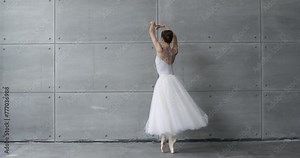 Elegant woman in a white tutu, dance ballet and perform choreographic elements on a gray background, rehearsal.