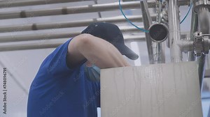 Dairy Food Production Factory. A Male Worker Wearing a Mask and a Cap is Intensely Cleaning the Equipment with a paper towel. Industrial Manufacturing Process. Complex Equipment. Human Labor
