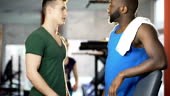 Male friends boasting of big strong muscles after workout in gym,...