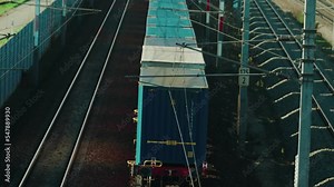 A slow freight train powered by electricity making its way through a rural area in Austria while being overtaken by a fast passenger train