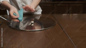 Maid meticulously wipes saucepan lid with rag in contemporary restaurant kitchen. Cook prepares restaurant kitchen for working day