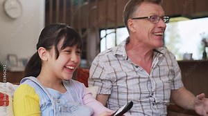 Grandfather and granddaughter together watch interesting entertainment media on TV. Old senior use technology communicate with young generation cross generation gap strengthen family bond. Divergence.