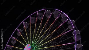 Ferris wheel at night. The multi-colored Illuminated wheel spins and rolls vacationers in its white booths