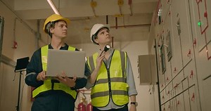 Two electricians electrical engineers in protective uniform checking voltage control panel screen system at electrical cabinet for generate electricity of factory in manufacture industrial