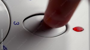 Pressing the old start button of a used analogue washing machine close up with a red power on indicator