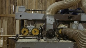 Carpenters opertes wood board running out carpenter jointer workbench at sawmill facility, lots of sawdust