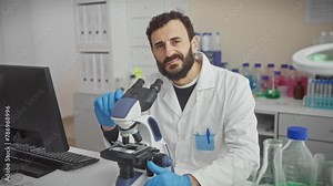 Bearded scientist examining specimens under microscope in modern laboratory setting.