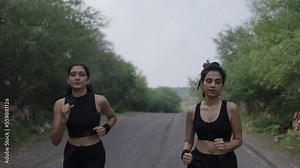 Two young India women jogging or running on road in nature, trees and Sunshine during the morning. healthy exercise Concept. Asian two girl jogging at fitness training. Sunlight around.