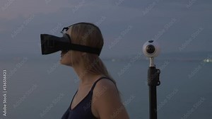 Woman using virtual reality glasses and camera shooting 360 degrees video nearby