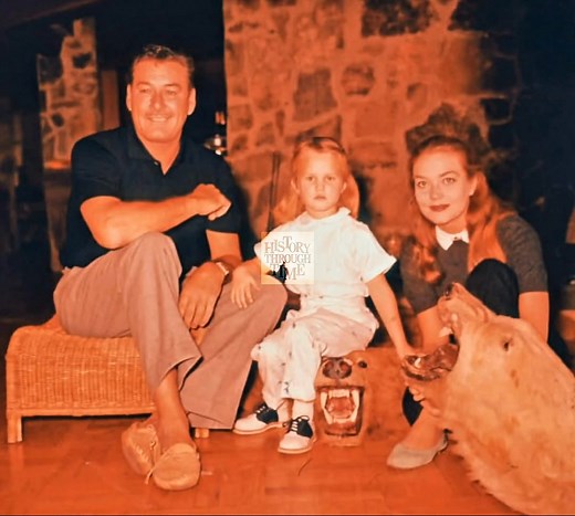 "Circa spring 1958, Errol Flynn and his third wife, Patrice Wymore, were photographed in a rare moment of tranquil domesticity with their young daughter, Arnella, at their lush estate near Port Antonio, Jamaica—a property Flynn had fallen in love with during filming years prior. The colonial-style home, nestled between banana groves and the Caribbean Sea, was a stark contrast to the frenzied pace of Hollywood, offering refuge for the aging swashbuckler, then 49, whose health and career were alre
