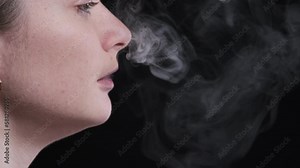 Beautiful girl smokes a red vape pod with replaceable cartridges on a black background. The concept of modern smoking, vaping and nicotine