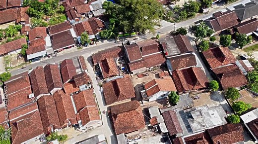 Aerial view of a traditional village with houses featuring red tiled roofs, surrounded by greenery and winding roads. The layout shows a mix of residential and communal spaces. Pati, Java, Indonesia.