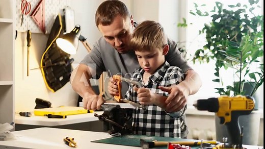 Carefully holding hacksaw, boy learns to cut metal under his fathers guidance. Working together in workshop, focus on precision and technique with each movement. Father and son concept