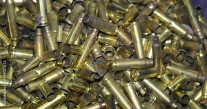 Close-up of empty bullet shells fall down on a pile of fired bullets, slow motion. Concept of too much violence, guns, crime and wars