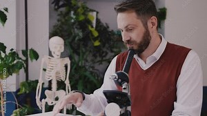 Male teacher use microscope and look through biology textbook in modern school. Young biology teacher prepares microscope for the lesson. High quality 4k footage