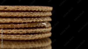 Close up view on traditional Dutch and Holland stroopwafels rotate or spin on a black mirror on a black background. Sweet waffle cookies lay on the table.