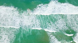 Scarica vista aerea della spiaggia di sabbia e della superficie dell'acqua. onde spumeggianti con il cielo. drone che vola sulla bellissima spiaggia tropicale. incredibile costa sabbiosa con onde bianche del mare. natura, paesaggio marino e concetto estivo. gratuitamente