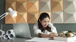Smart interior designer using laptop analysis building structure with project plan, laptop and architectural model at modern office. Asian project manager measures building design. Manipulator.