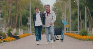 Dad helps disabled son to go, family support. Disabled guy walking down the road.