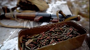 A box of machine gun ammo. There are a lot of machine gun ammo on the table. A grenade launcher is lying next to a box of ammo on a table in a field on a military training ground