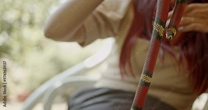 A woman sits outside with a red milk snake. She interacts and plays with the snake.
