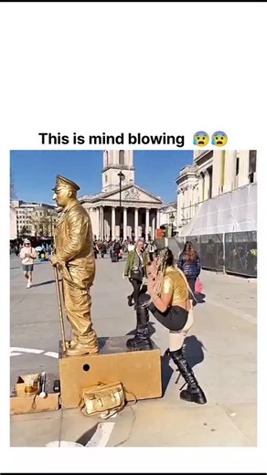Explore World on Instagram: "The post features a viral video of contortionist Zack D. Films performing as a gold-painted "living statue" in London's Trafalgar Square, executing extreme bends like self-sitting on his head to stun onlookers. With over 8 million views and 24,000 likes in under 24 hours, it taps into the timeless fascination with street illusions, blending body art, yoga-inspired flexibility, and surprise for broad appeal. Replies debunk the feat using hidden metallic rods and hinge