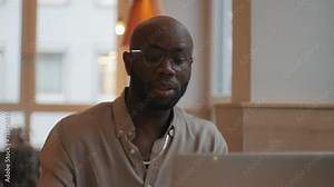 A young African American man is looking at a webcam and making a video call. Confident man talking and conducting online video chat interview, sitting at table and drinking coffee