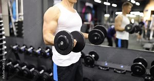 Fit and muscular man is training with heavy dumbbells in gym. Male bodybuilder training in gym and lifting dumbbell with hand