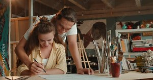 Caucasian young handsome man painter teaching how to draw with a pencil an outline a pretty woman at the art class in the studio.