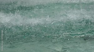 Close-up view of drops and splashes of water in a fountain. The blue water in the fountain shimmers and shines.