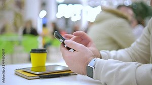 A person is happily enjoying their coffee while using a smartphone and simultaneously jotting down notes in a notebook