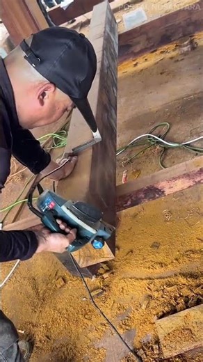 smoothing the surface of a long thick wooden beam using a power hand planer in a carpentry workshop