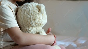 The children sit on the bed and play with the teddy bear.