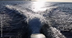 The view from the sea of the engine of a moving boat, closeup. Shiny waves and ripples on the water
