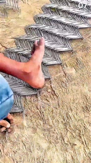 Unrolling chain-link fencing material manually on outdoor ground.