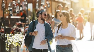 Couple stroll down sunny street with coffee - Free Stock Video